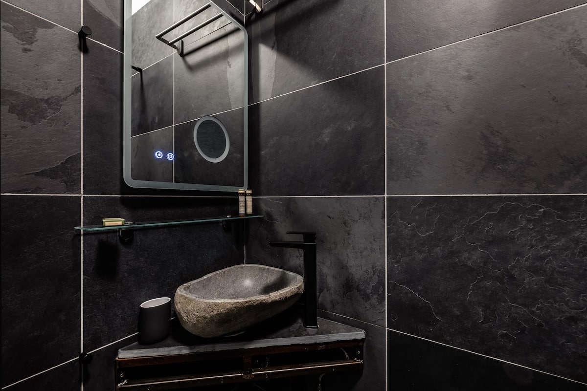 A modern bathroom with a stone sink, black fixtures, and a glass shelf.