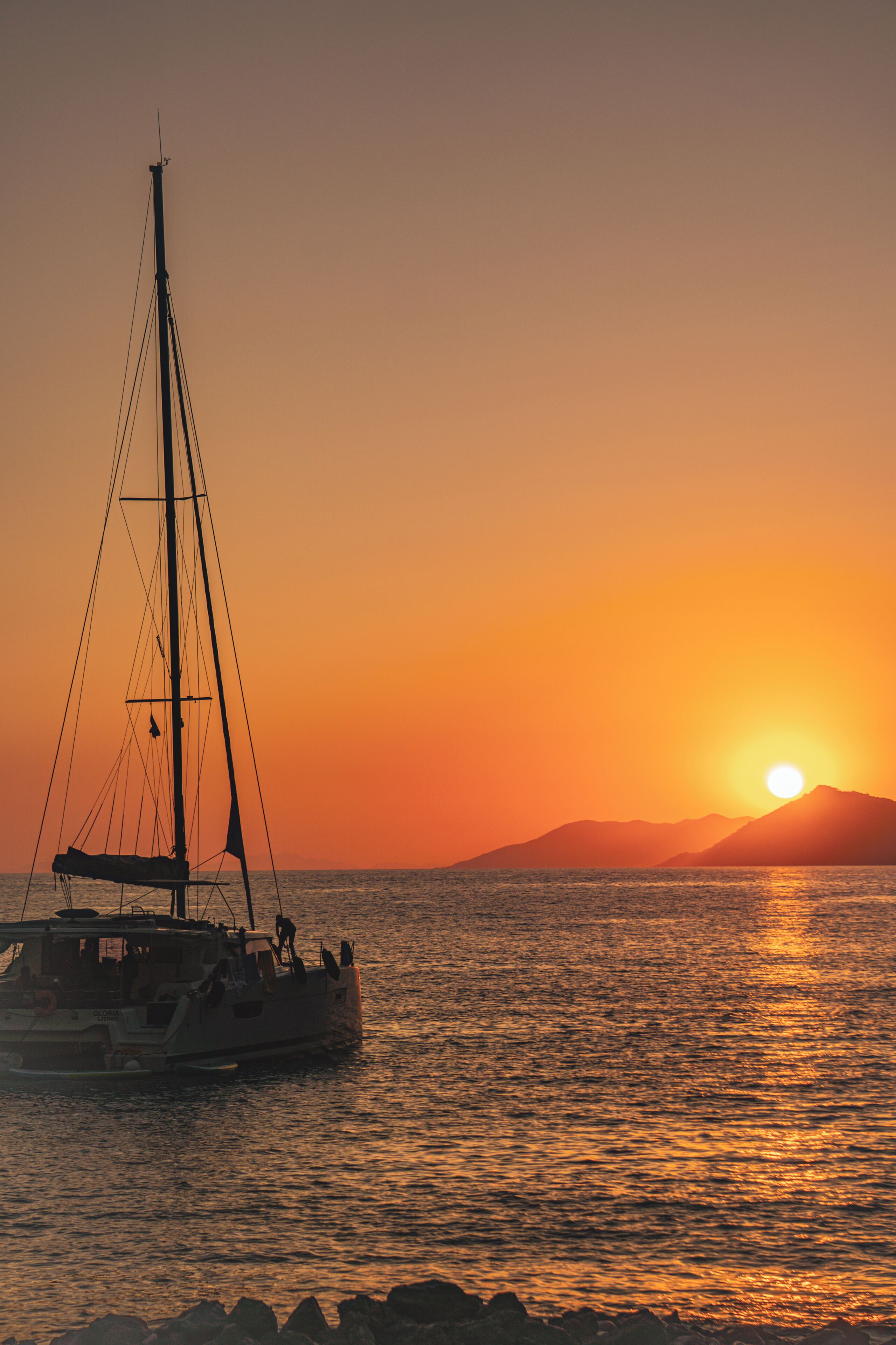 Un voilier sur des eaux calmes, au coucher du soleil, sous un ciel dégagé.