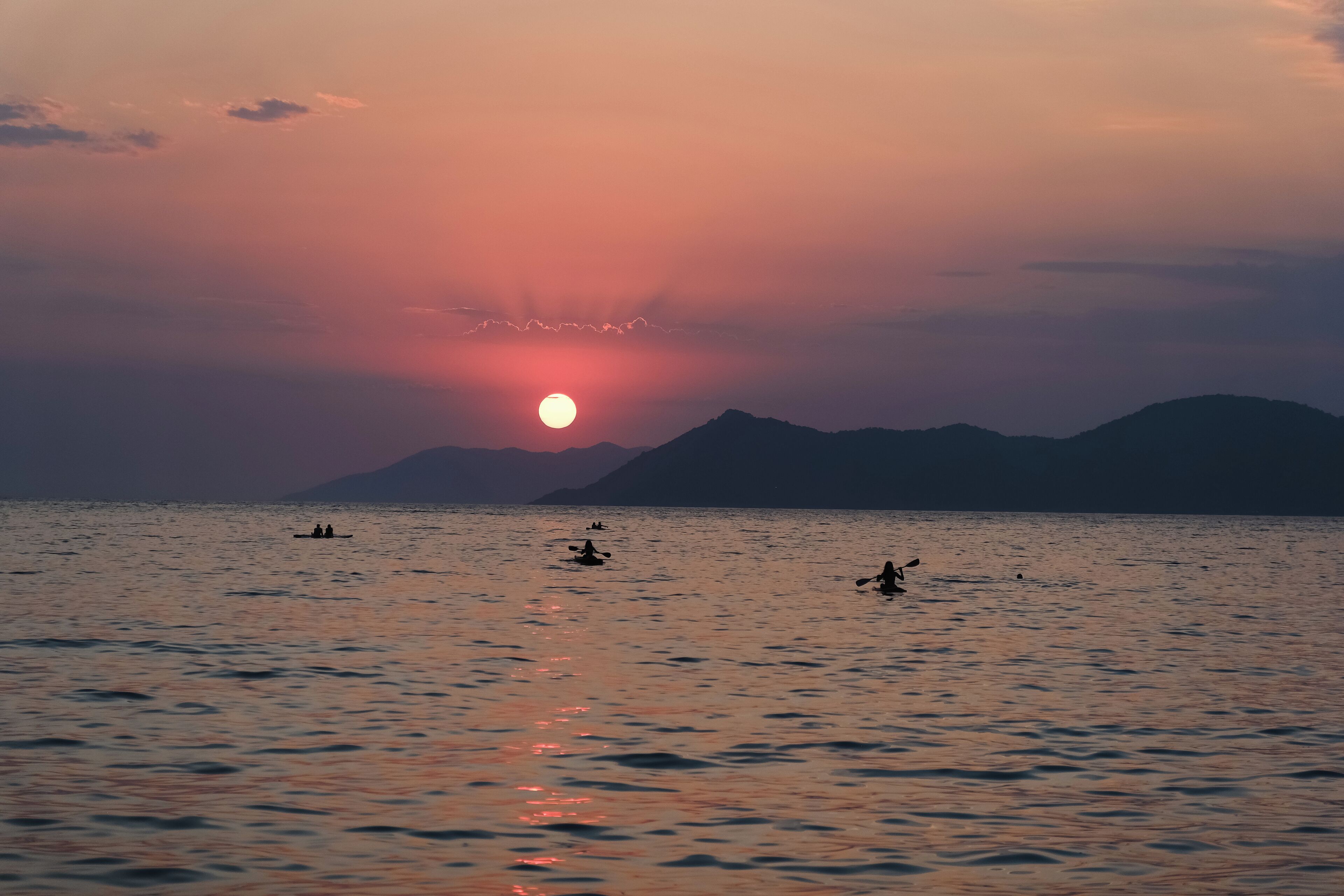 A sunset over a calm sea with boats and distant mountains.