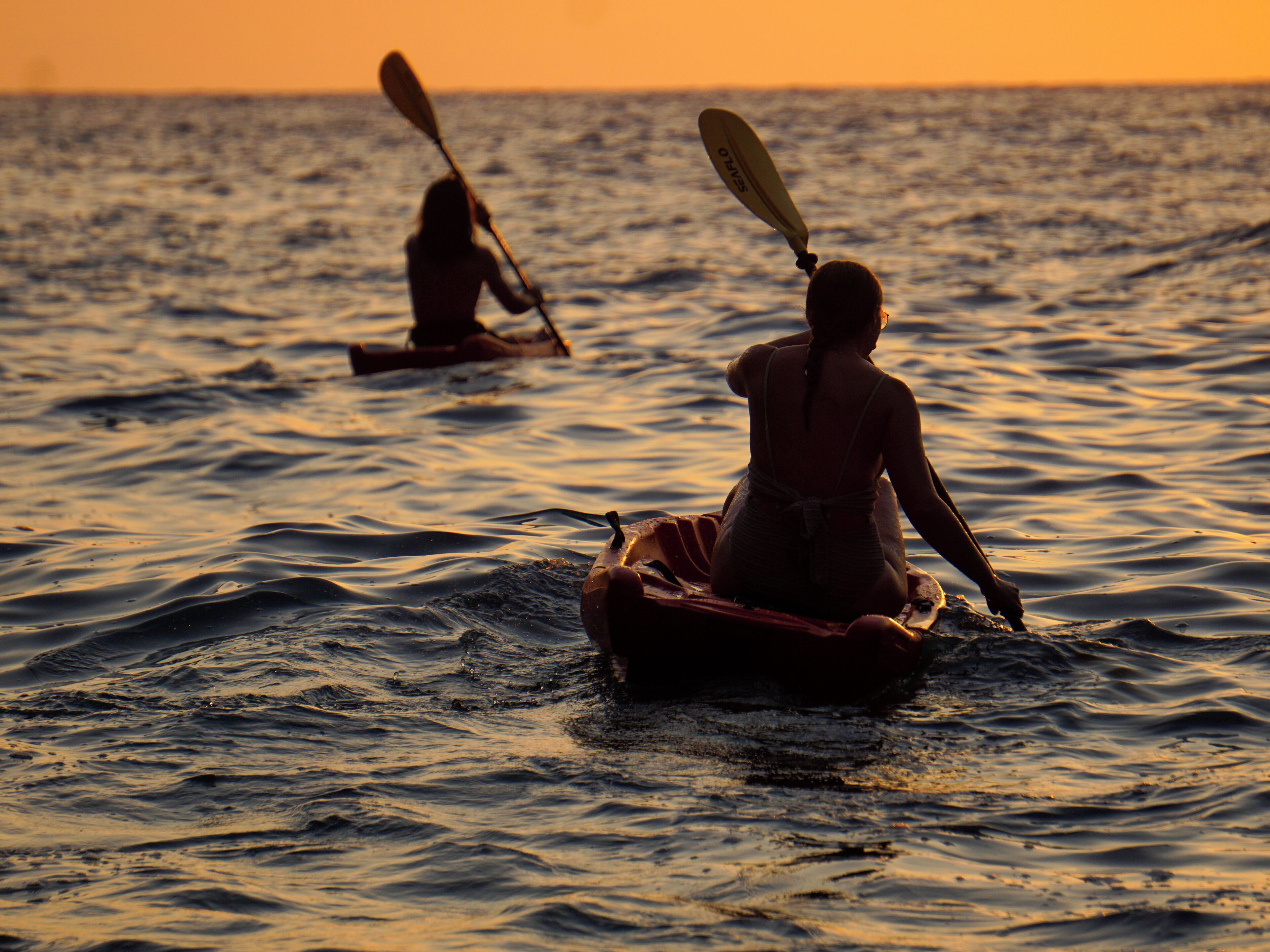 Deux personnes pratiquent le kayak sur une mer calme au coucher du soleil.