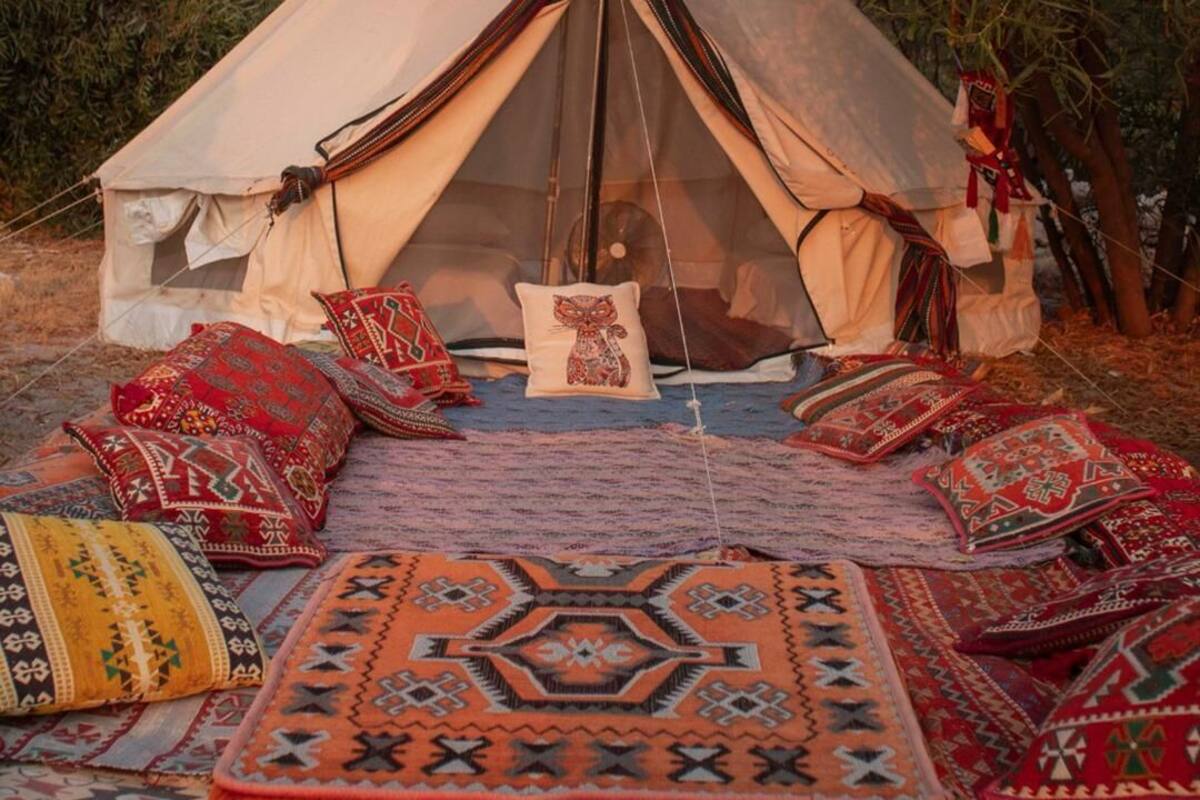 A tent with a view of a mountainous landscape, surrounded by colorful rugs and pillows.