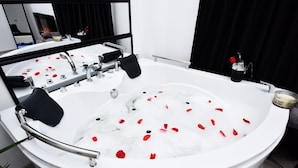 A white freestanding bathtub with rose petals floating in the water, a black towel, and a bottle of lotion. - Lux: Jacuzzi Semineu Pat Rotund Oglinda Tavan (Craiova, Preajba)