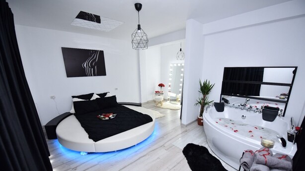A modern bedroom with a circular bed, a large mirror, a bathtub with rose petals, and a vanity with a mirror. - Lux: Jacuzzi Semineu Pat Rotund Oglinda Tavan (Craiova, Preajba)