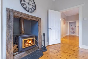 A room with a stone fireplace, a clock, and a wooden floor. - Sunshine Cottage with a private garden (Katoomba)