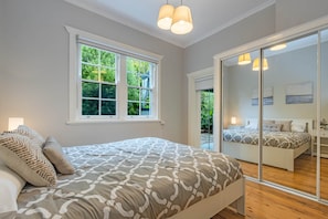 A bedroom with a large bed, a window with a view of greenery, and a sliding glass door leading to an outdoor area. - Sunshine Cottage with a private garden (Katoomba)