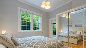A bedroom with a large bed, a window with a view of greenery, and a sliding glass door leading to another room. - Sunshine Cottage with private garden, Katoomba (Katoomba)