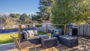 An outdoor deck with wicker furniture, a grill, and a view of a house in the background. - Sunshine Cottage with private garden, Katoomba (Katoomba)