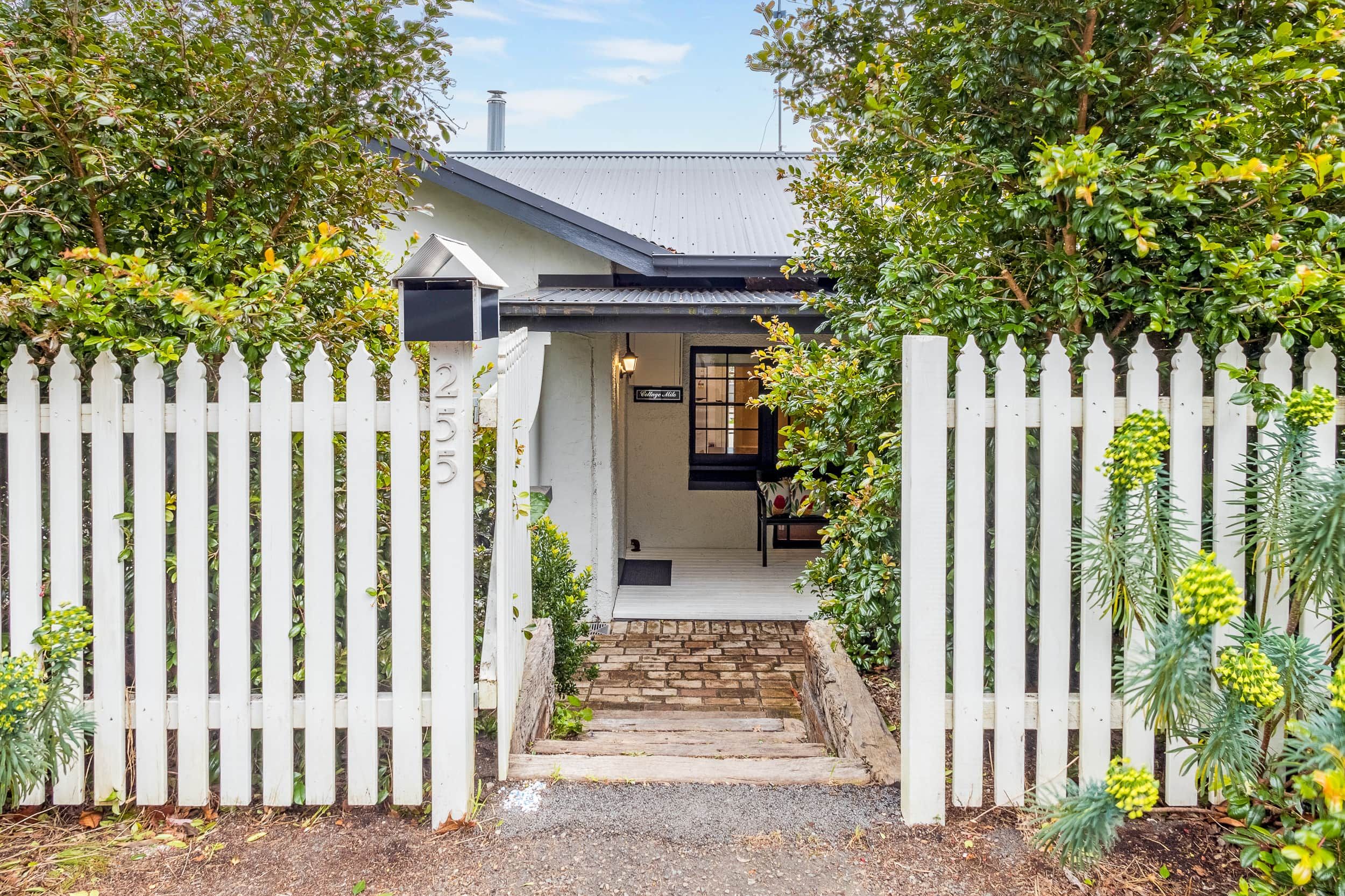 A house with a white picket fence, a stone pathway leading to the entrance, and a sign indicating 'Cottage Hill.'