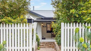 A house with a white picket fence, a brick pathway leading to the entrance, and lush greenery around. - Sunshine Cottage with private garden, Katoomba (Katoomba)