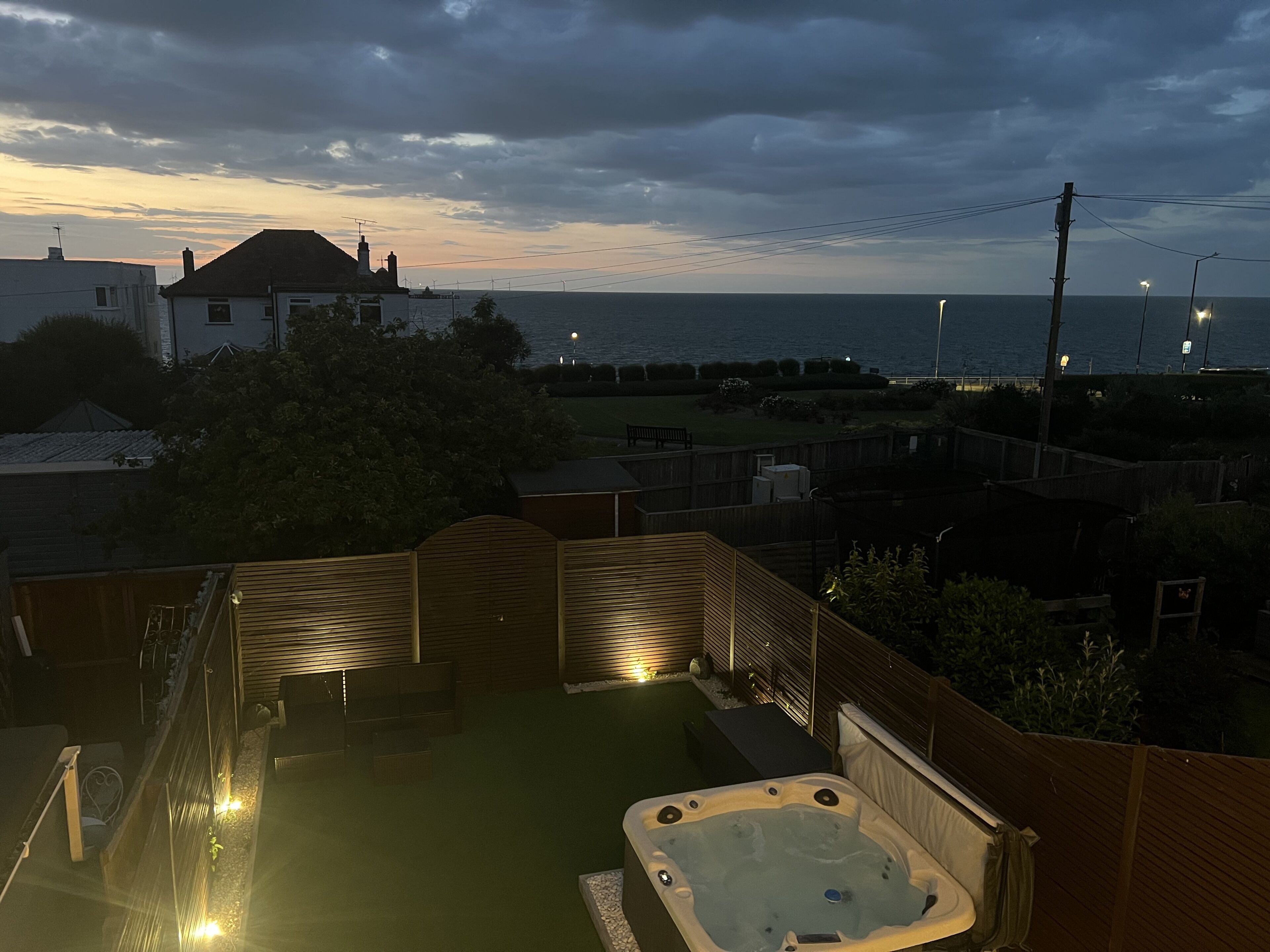 Uma banheira de hidromassagem num quintal com vista para o mar e uma casa ao fundo.