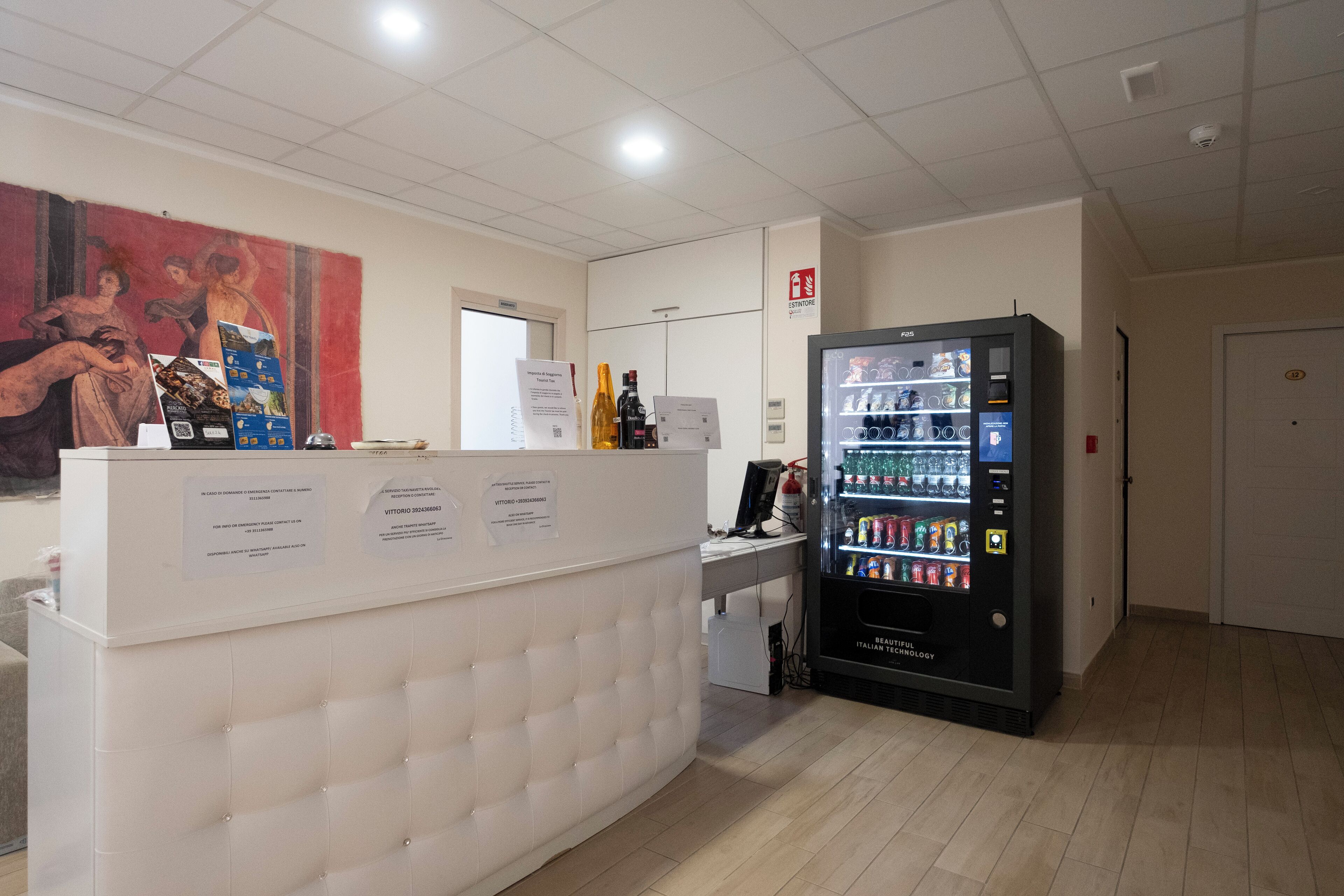 A reception area with a tufted white counter, a beverage vending machine, and a red mural on the wall.