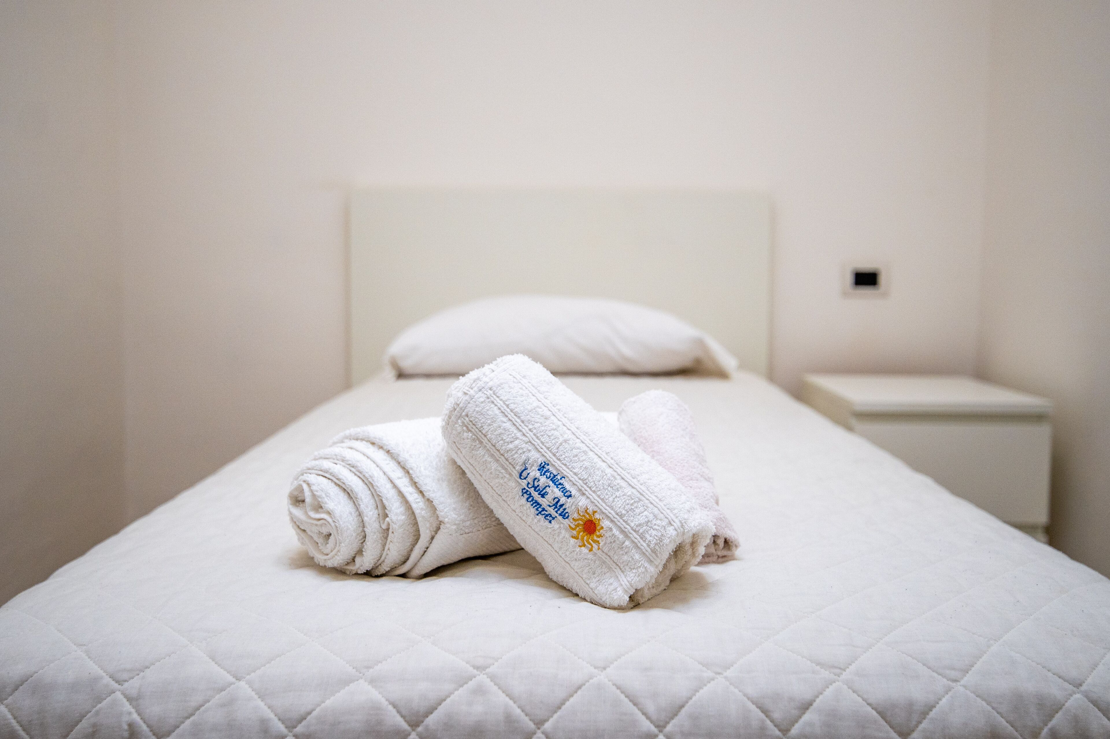 A neatly made bed with a quilted white bedspread and two rolled towels with embroidered text.