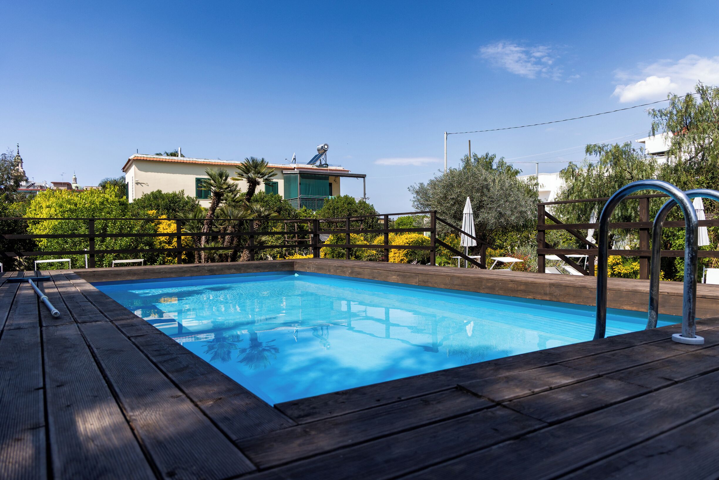 A swimming pool with a wooden deck, surrounded by a fence and trees.
