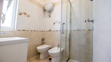A bathroom with a toilet, bidet, and glass-enclosed shower.