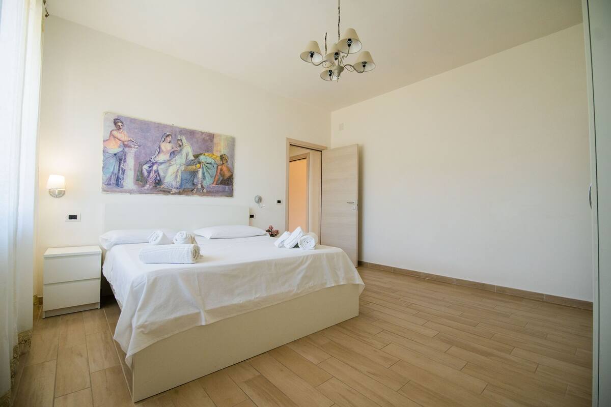 Ein Schlafzimmer mit Bett, Nachttisch, Gemälde und Tür.