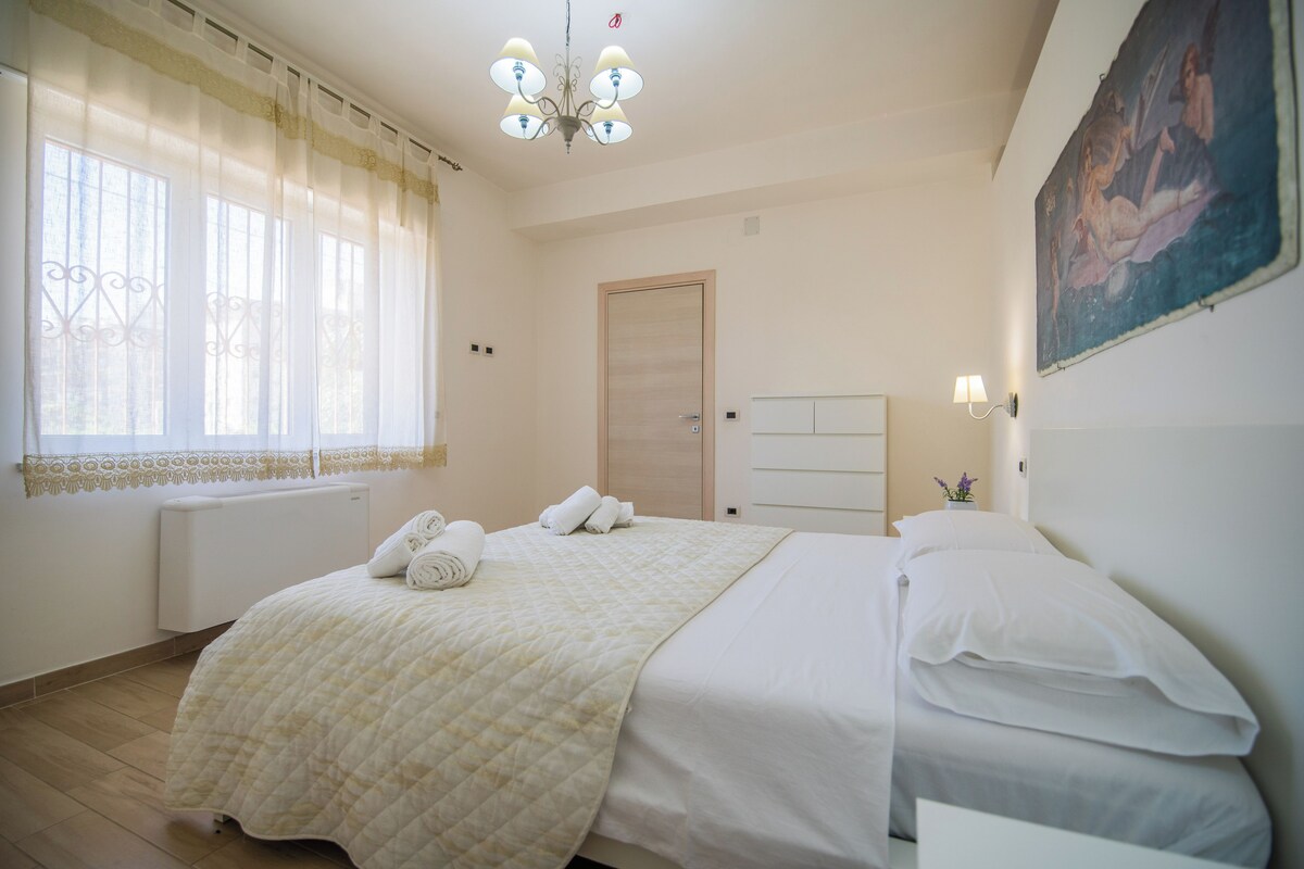 Un dormitorio con una cama, un radiador, una puerta, una araña y un cuadro en la pared.