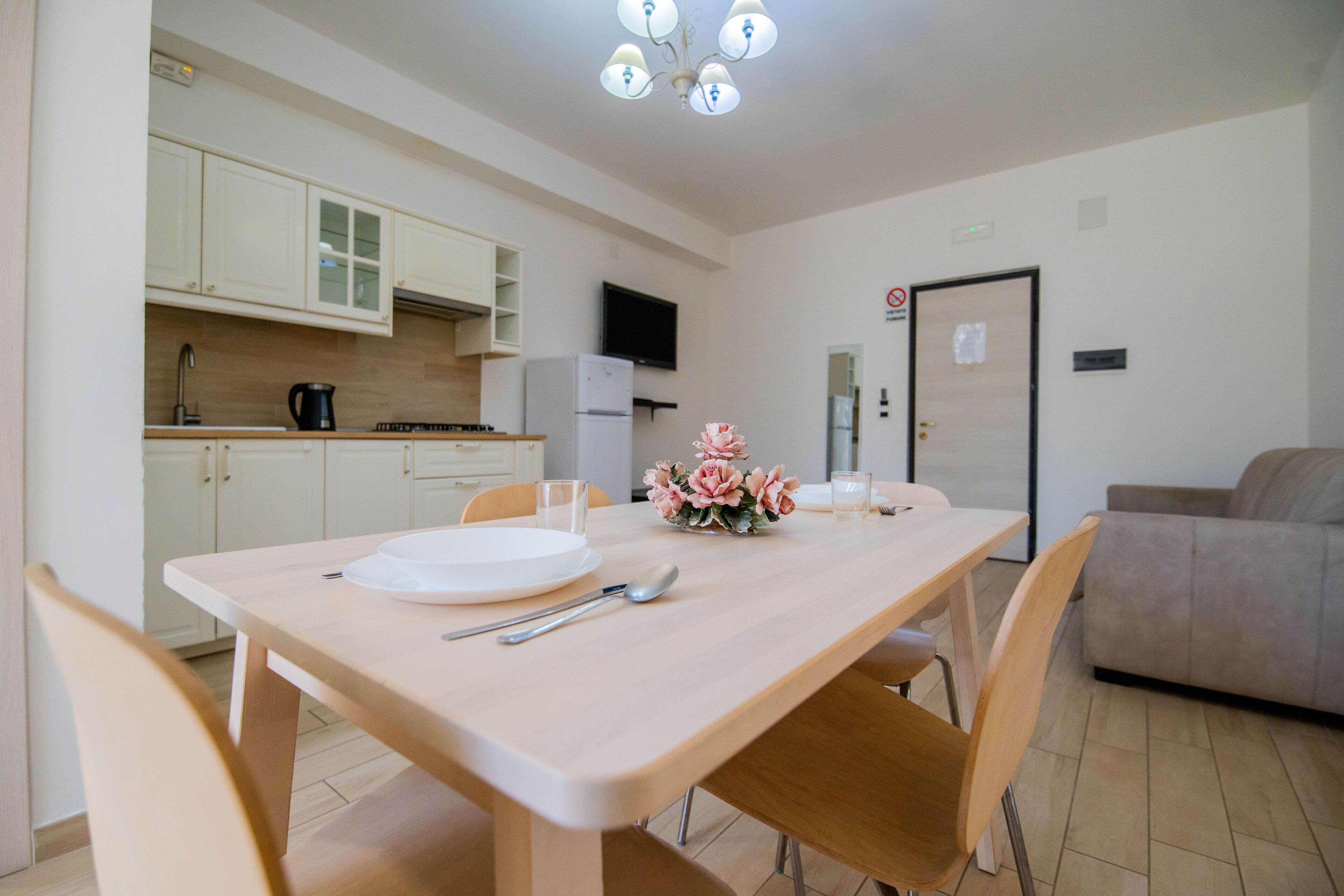 Una cocina moderna con armarios blancos, una mesa de comedor dispuesta con platos, cubiertos y un jarrón de flores.