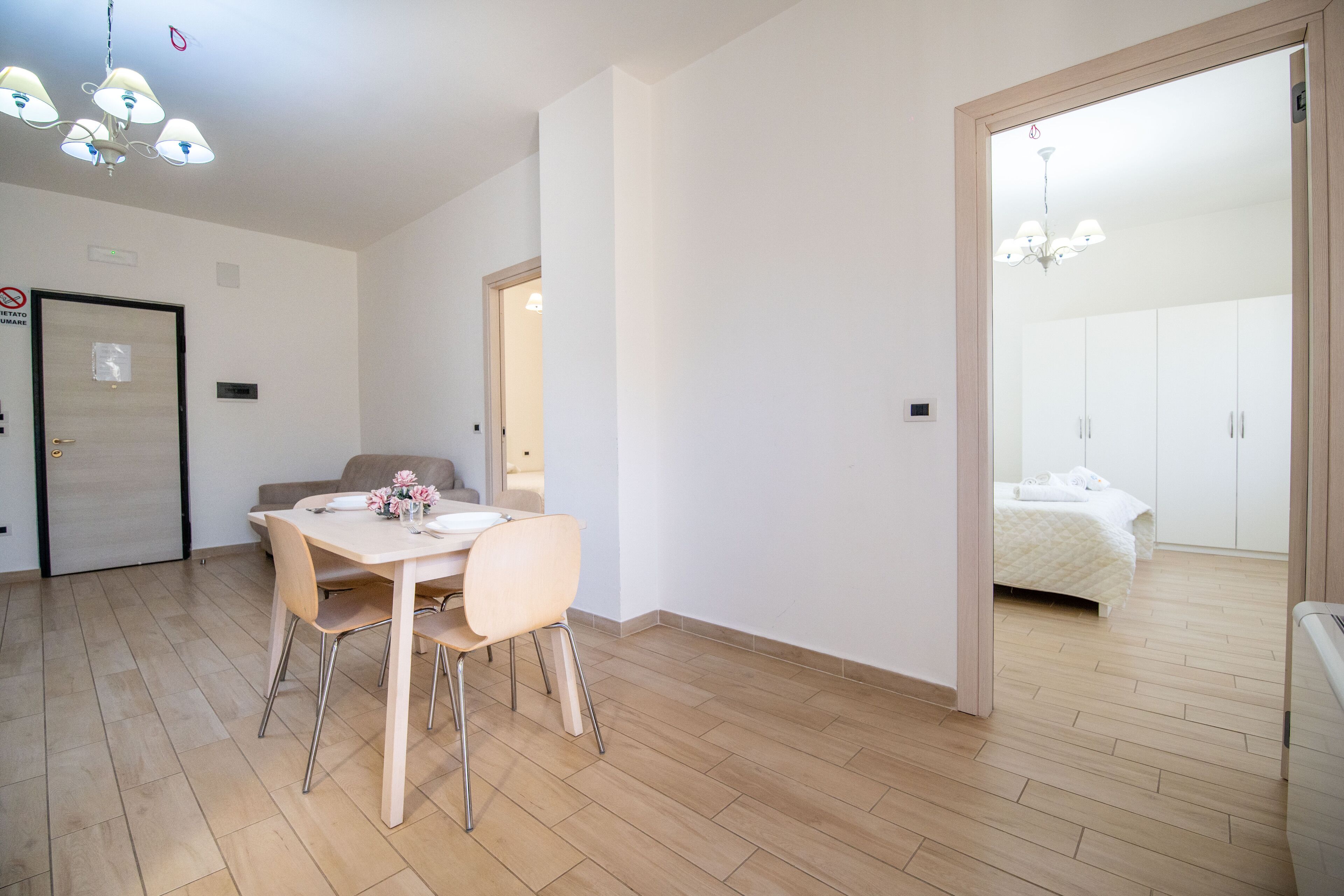 A modern, well-lit room with a dining table and chairs, a sofa, and a bed with a white duvet.