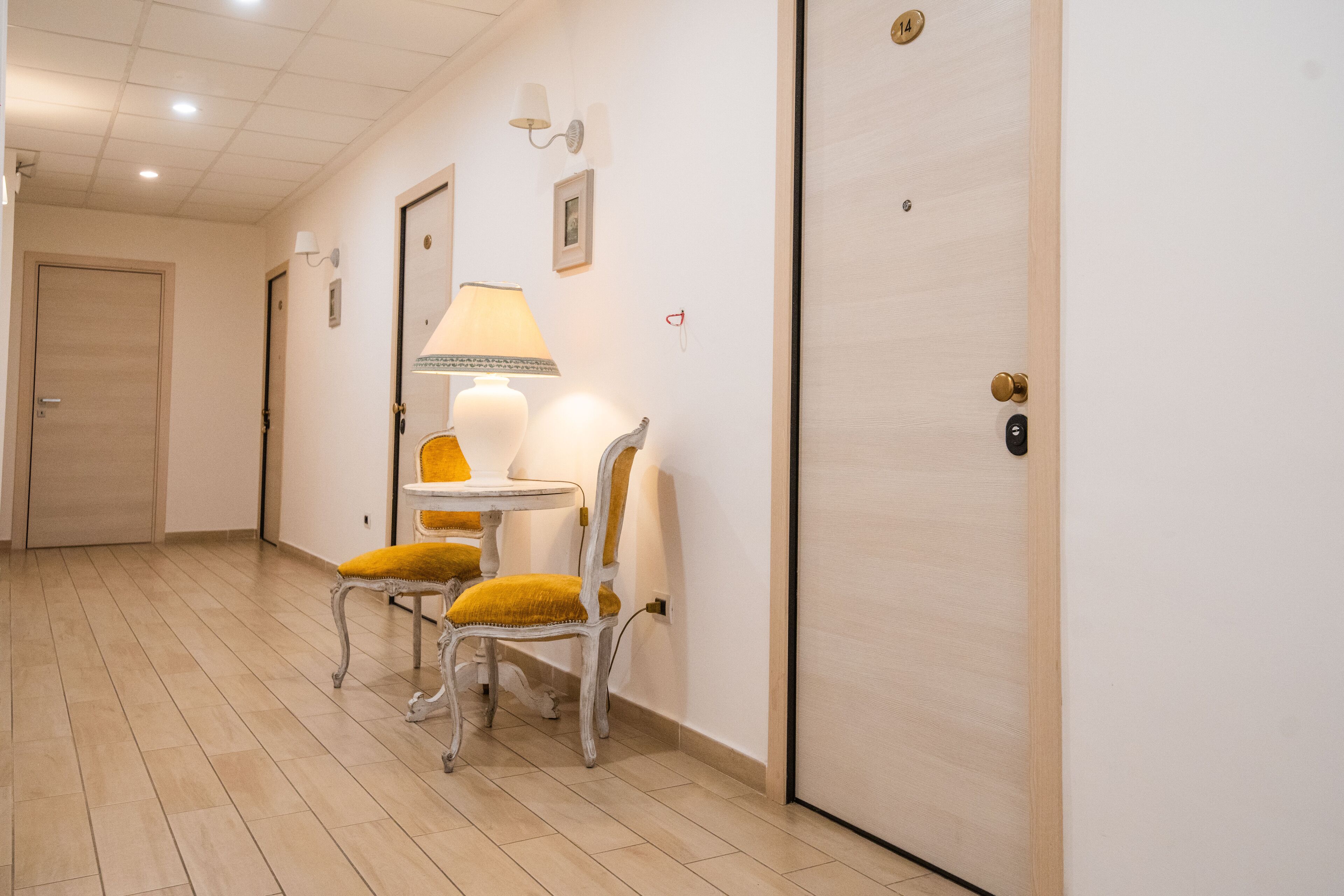 A hallway with a door, a lamp, and two chairs with yellow cushions.