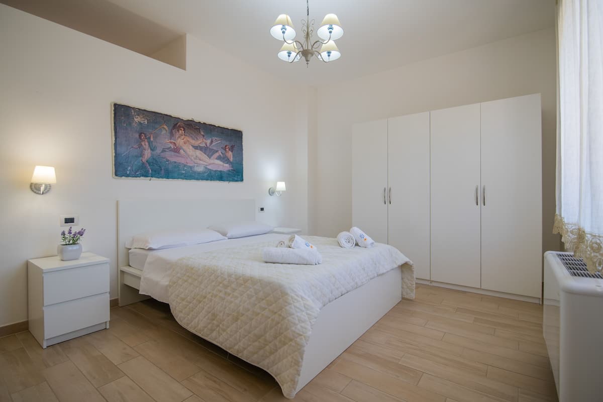 Ein Schlafzimmer mit Bett, Nachttischen, einem Gemälde, einer Chandelier und einem Kleiderschrank.