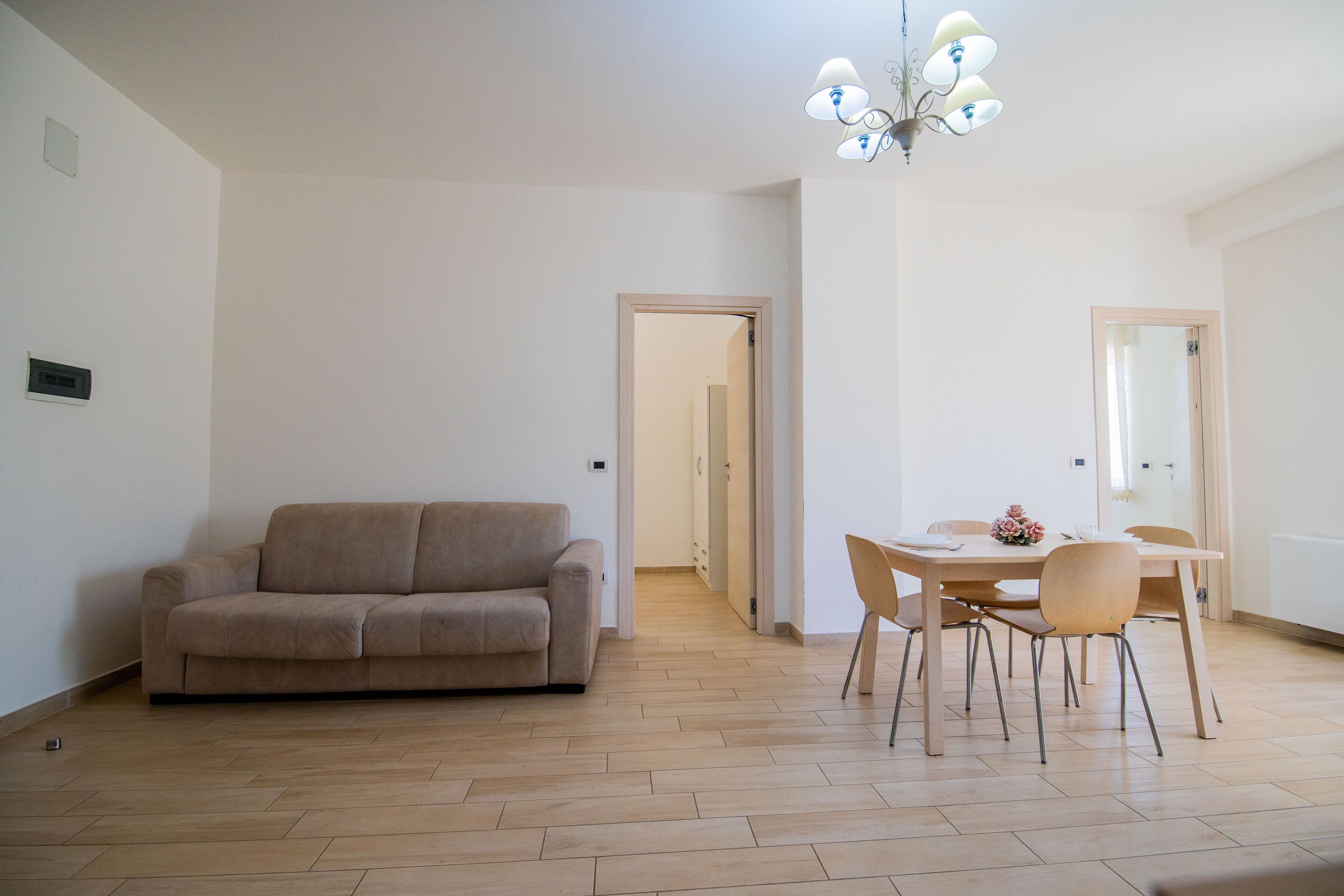 A spacious living area with a beige sofa, a wooden dining table with chairs, and a chandelier.