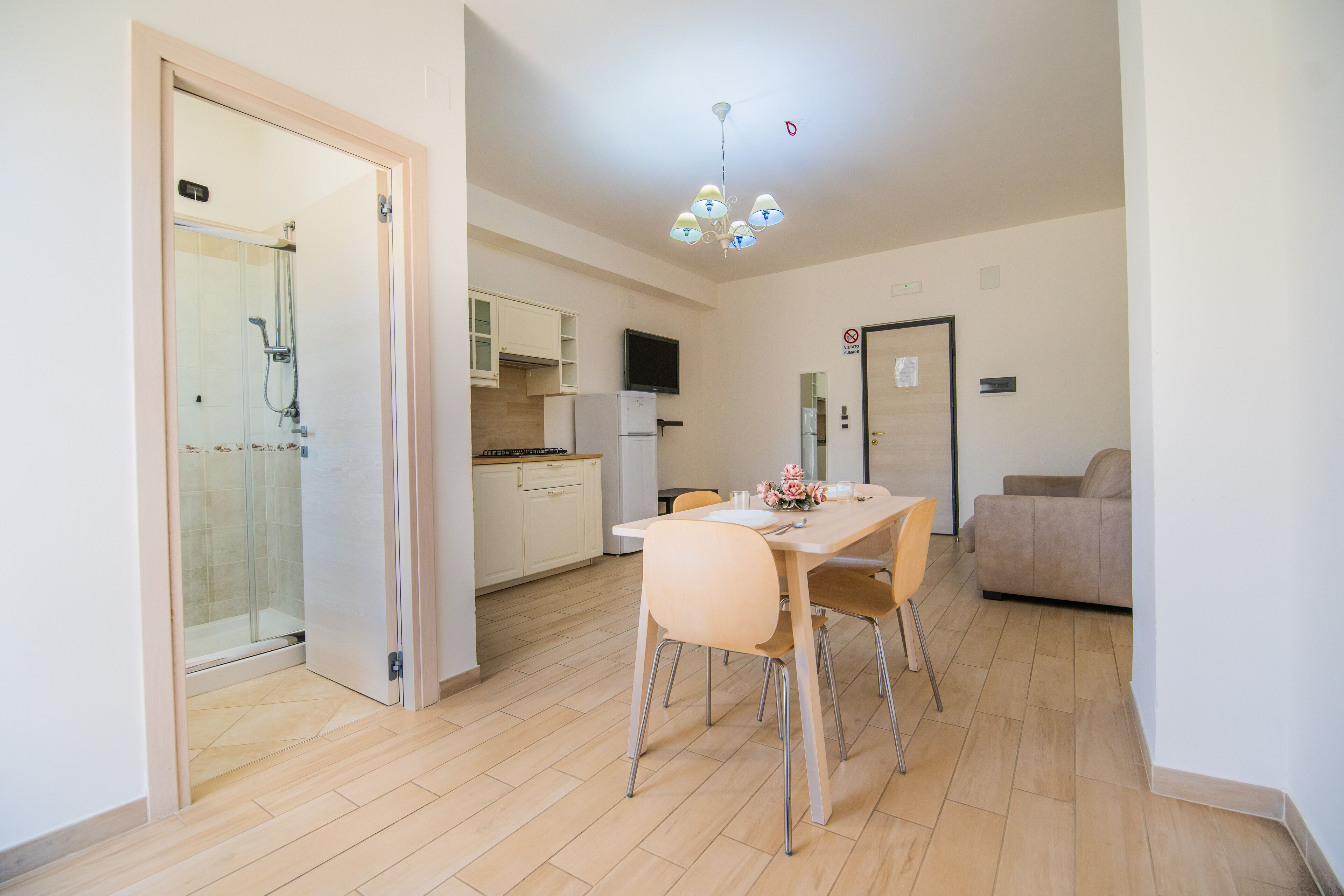 A modern kitchen with a dining area, a sofa, and a glass shower enclosure.