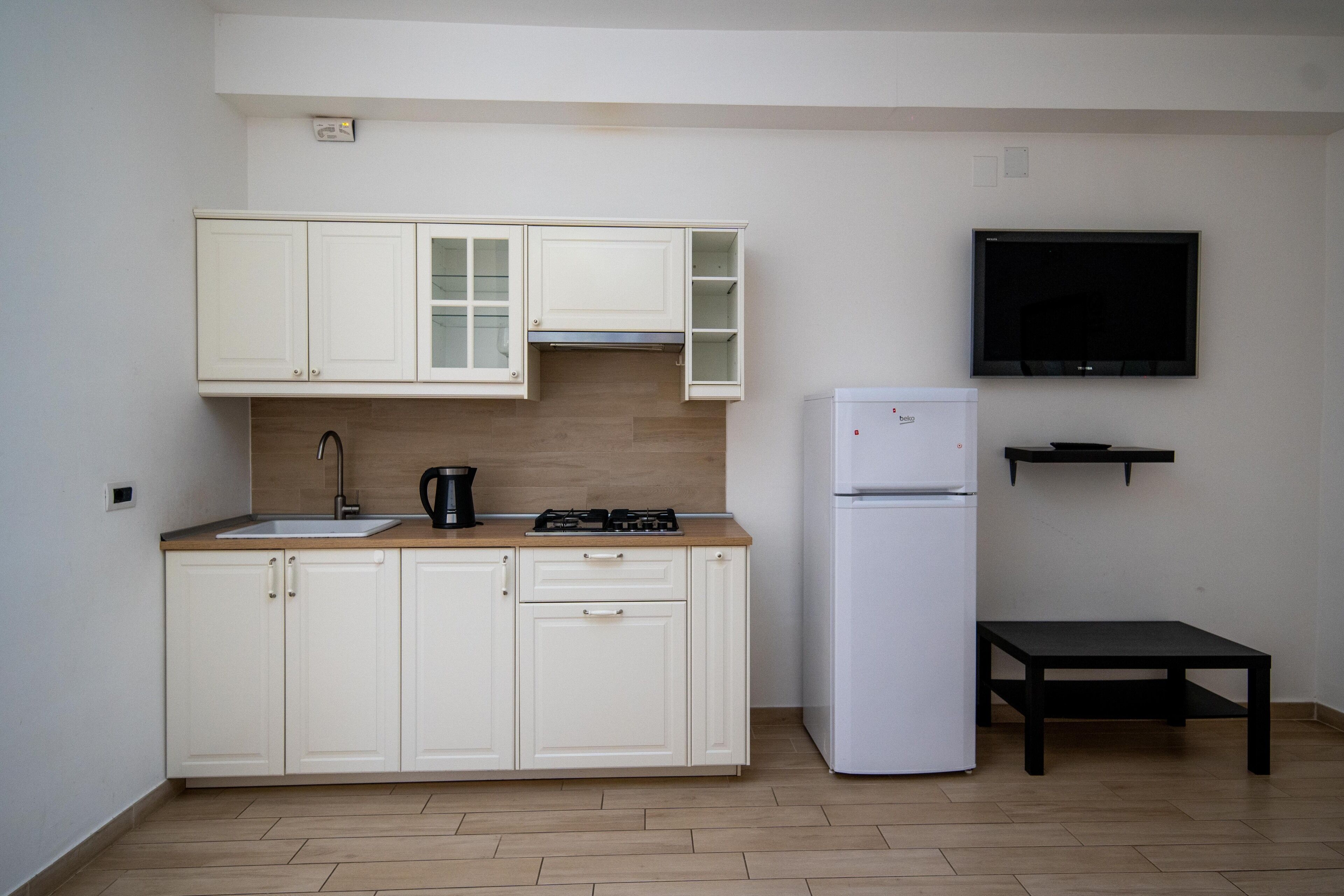 A compact kitchen with white cabinets, a sink, a stove, and a refrigerator.
