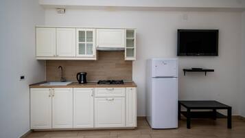 A compact kitchen with white cabinets, a sink, a stove, and a refrigerator.