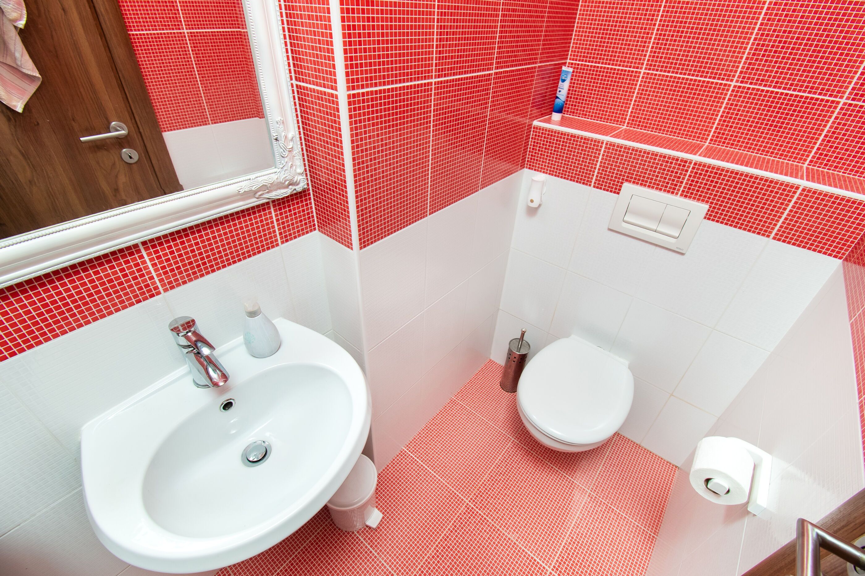 A bathroom with a white sink, a toilet, and red-tiled walls.