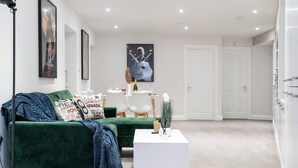 A modern living room with a green sofa, a white coffee table, and a dining area in the background. - Livestay - 2 Bed Hollywood Movie Themed Apt (Barnet)
