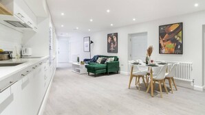 A modern kitchen with white cabinets and a dining area with a green sofa and white chairs. - Livestay - 2 Bed Hollywood Movie Themed Apt (Barnet)