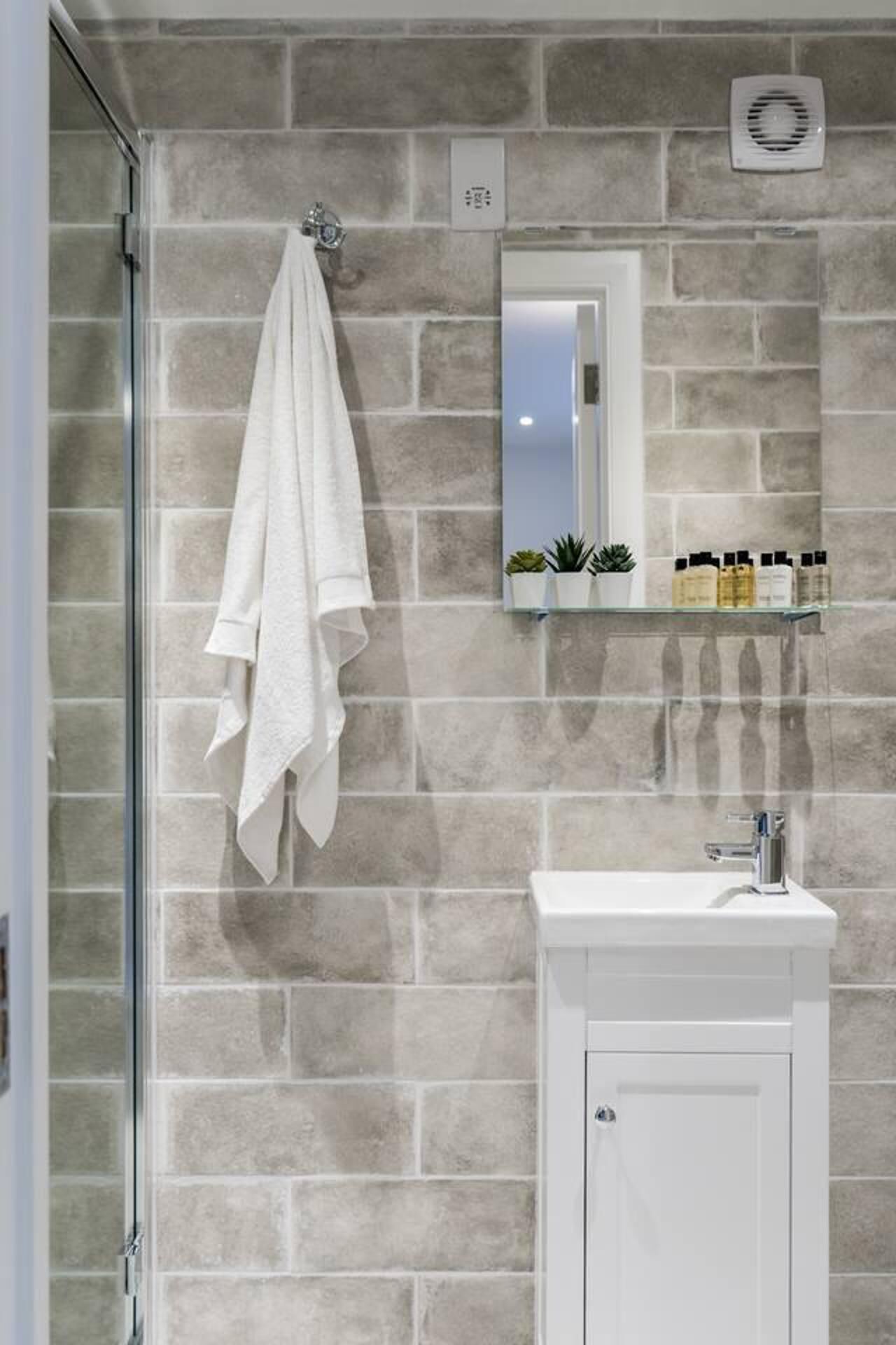 A bathroom with a stone wall, a white sink, a mirror, and a towel hanging on a rack.