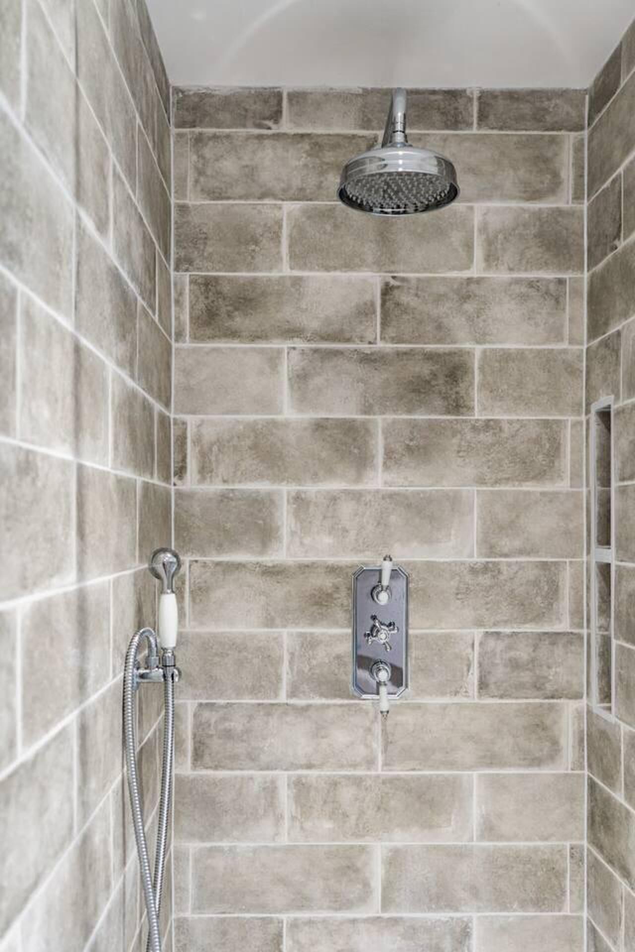 A shower with a handheld showerhead and a wall-mounted control panel.