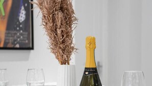 A dining table set with plates, cutlery, a bottle of Prosecco, a jar of jam, and a vase with dried plants. - Livestay - 2 Bed Hollywood Movie Themed Apt (Barnet)