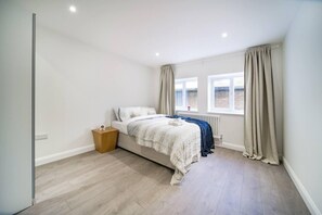 A bedroom with a bed, a bedside table, a window with curtains, and a radiator.