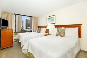 Habitación de hotel con dos camas, un televisor, una ventana con vista a la ciudad y un cuadro en la pared.
