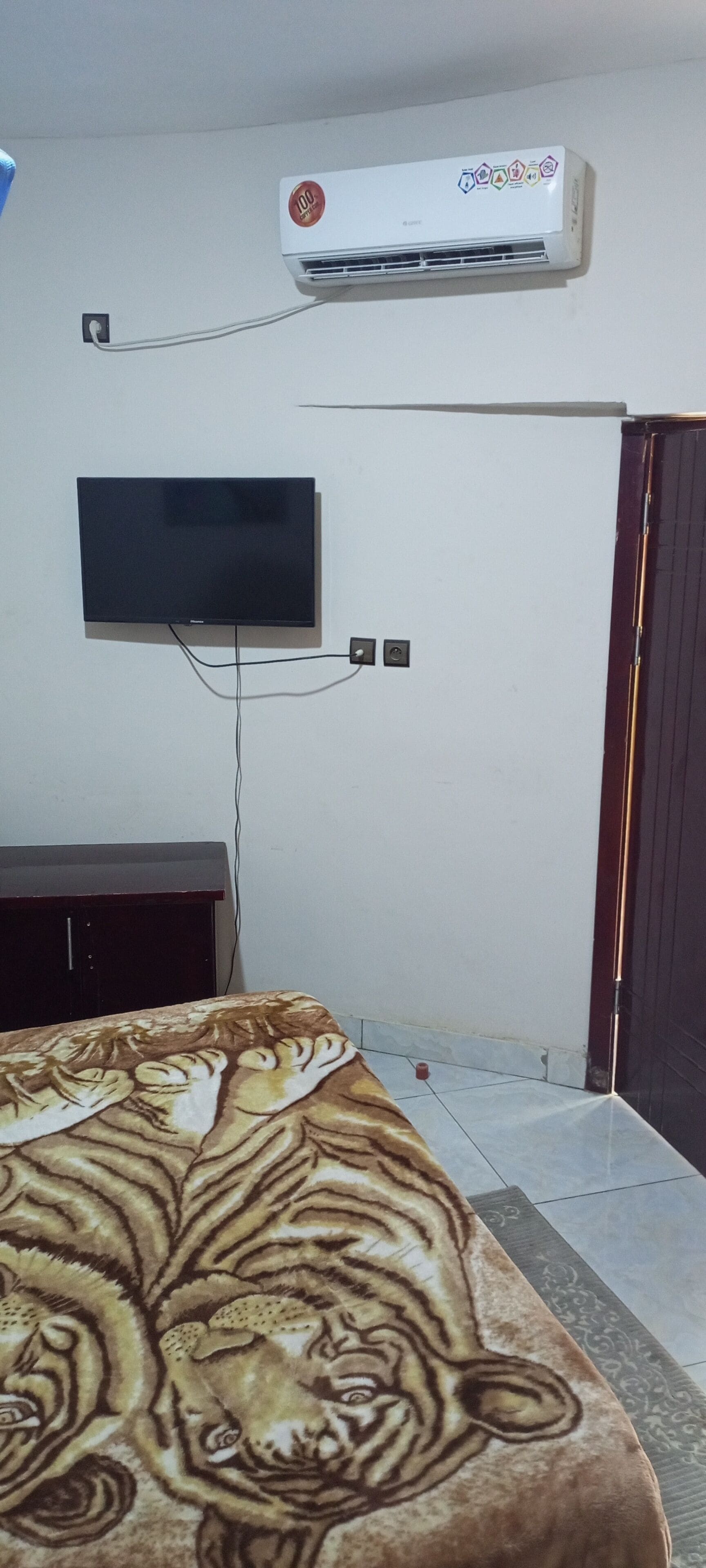 Un dormitorio con cama, televisor de pantalla plana en la pared, aire acondicionado y armario de madera.