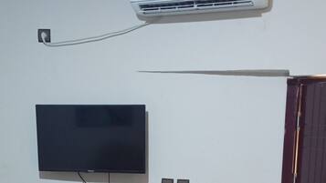 Un dormitorio con cama, televisor de pantalla plana en la pared, aire acondicionado y armario de madera.