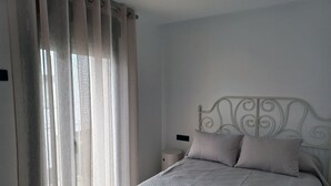 Een slaapkamer met een bed, gordijnen, een nachtkastje en een wandlamp.