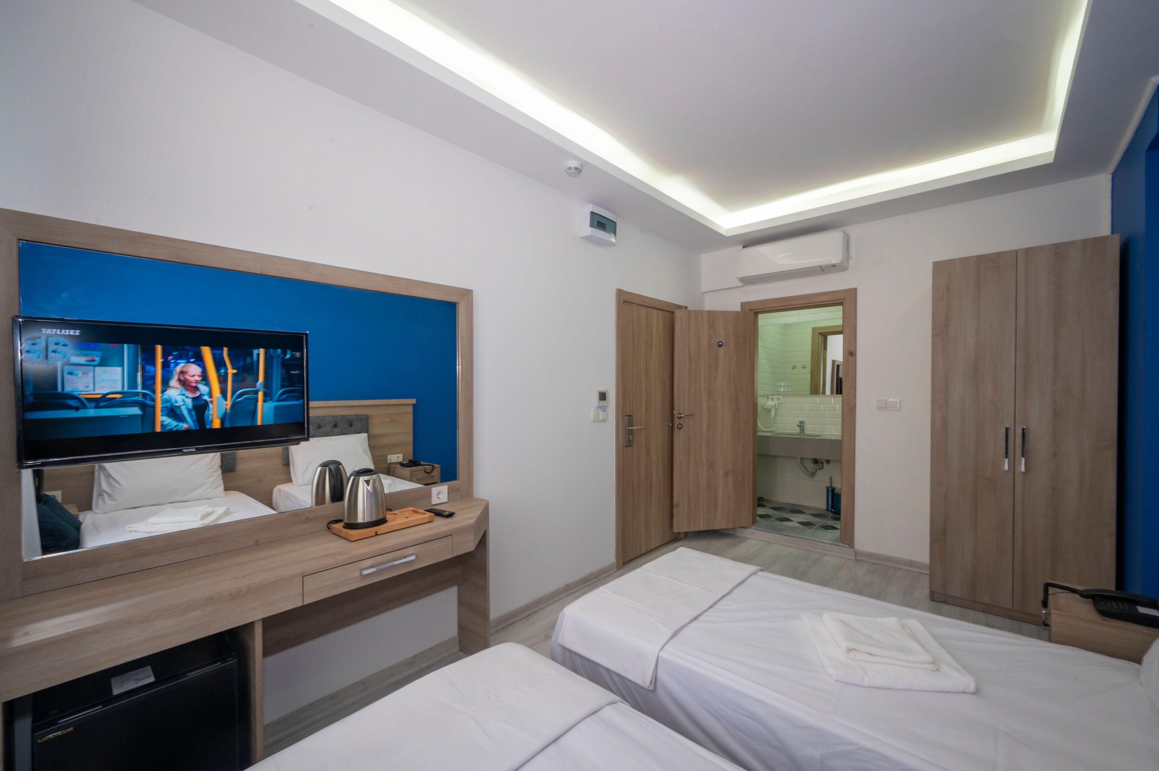 A hotel room with a bed, a desk with a TV, a wardrobe, and a bathroom visible through an open door.