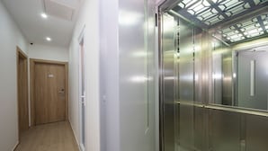 Un pasillo con una puerta de madera con el letrero "104" y un ascensor con panel de vidrio.