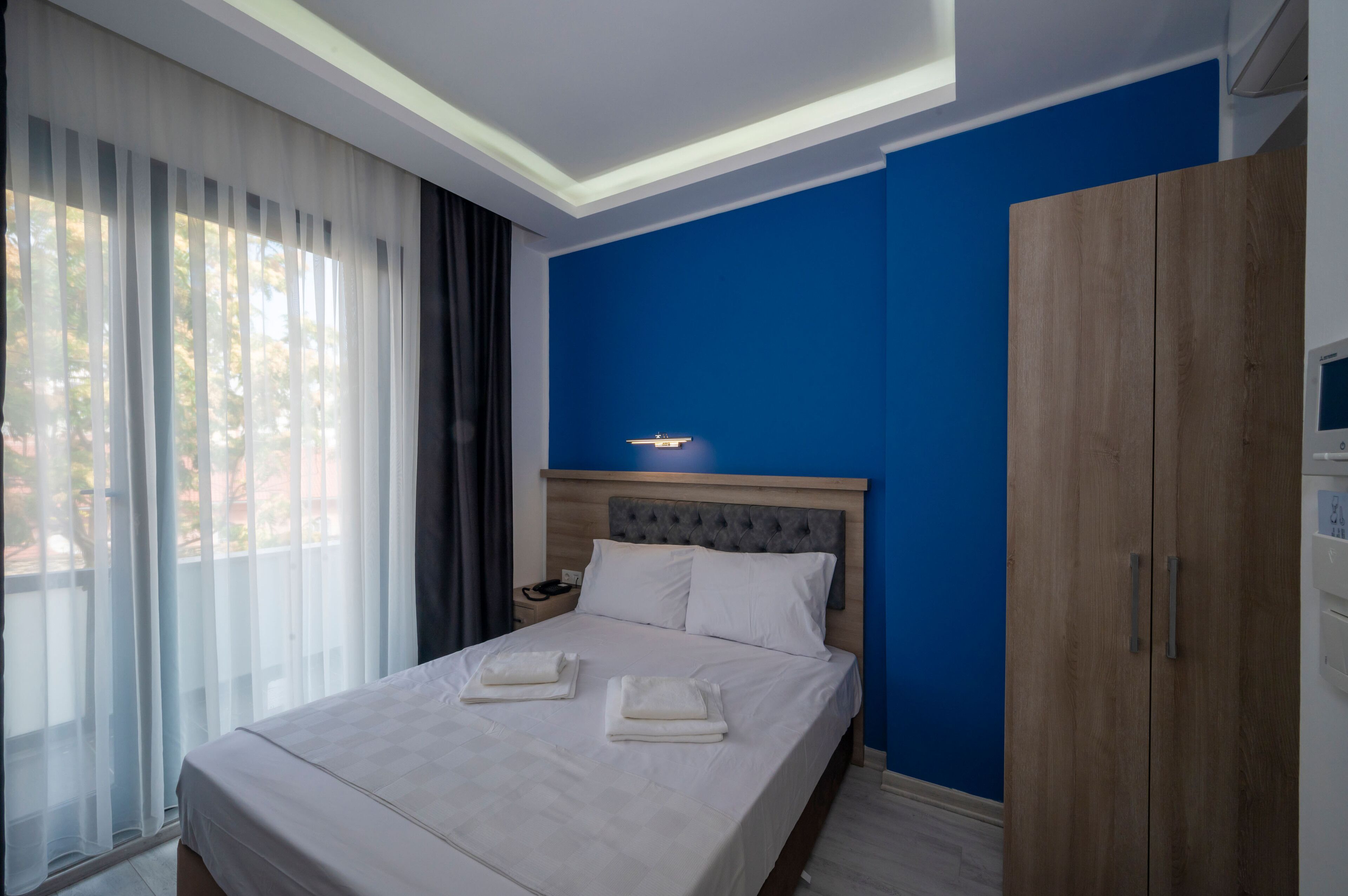Une chambre d’hôtel avec un lit, une table de chevet, une armoire et une fenêtre avec des rideaux.