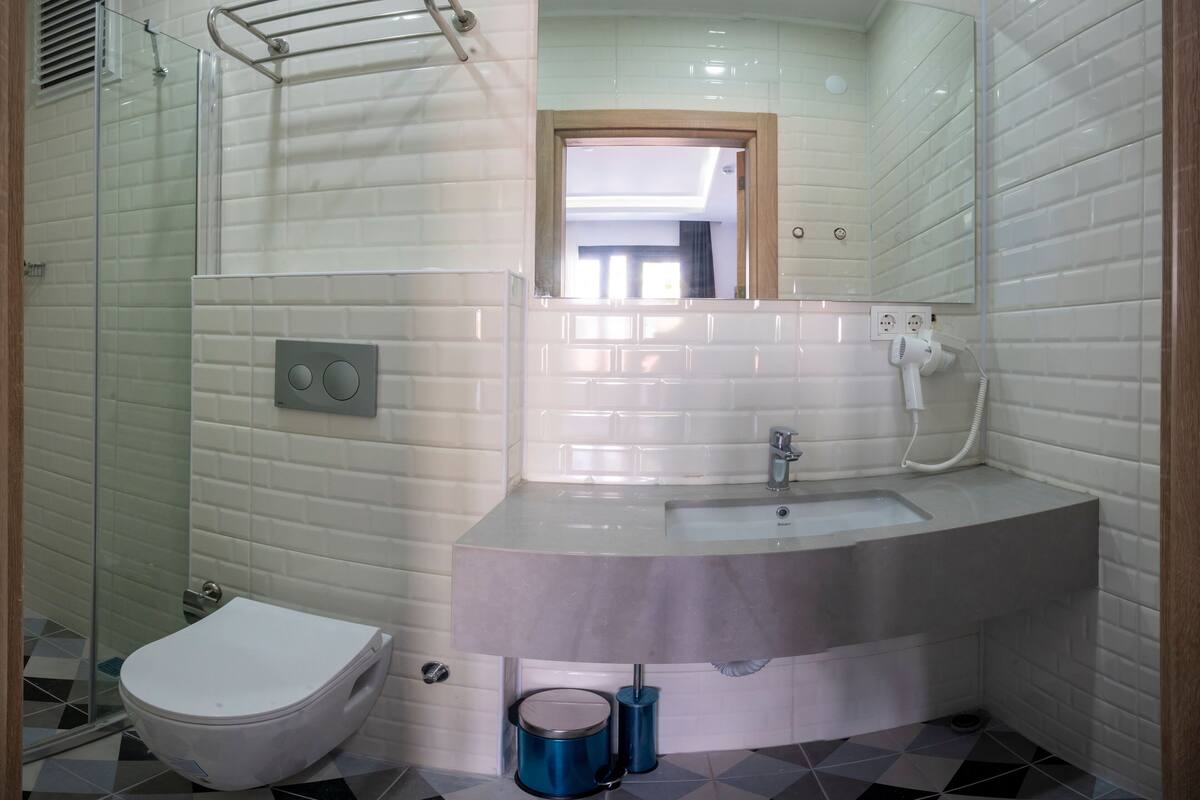 A modern bathroom with a glass shower enclosure, a white toilet, a sink with a mirror above it, and a tiled floor.