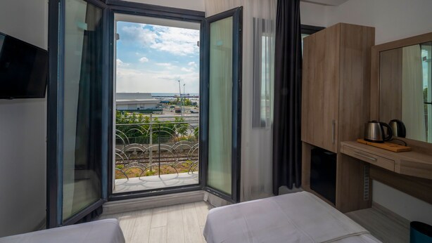 Una habitación de hotel moderna con un amplio ventanal corredero que da a un balcón, una cama, un armario de madera y un televisor de pantalla plana.