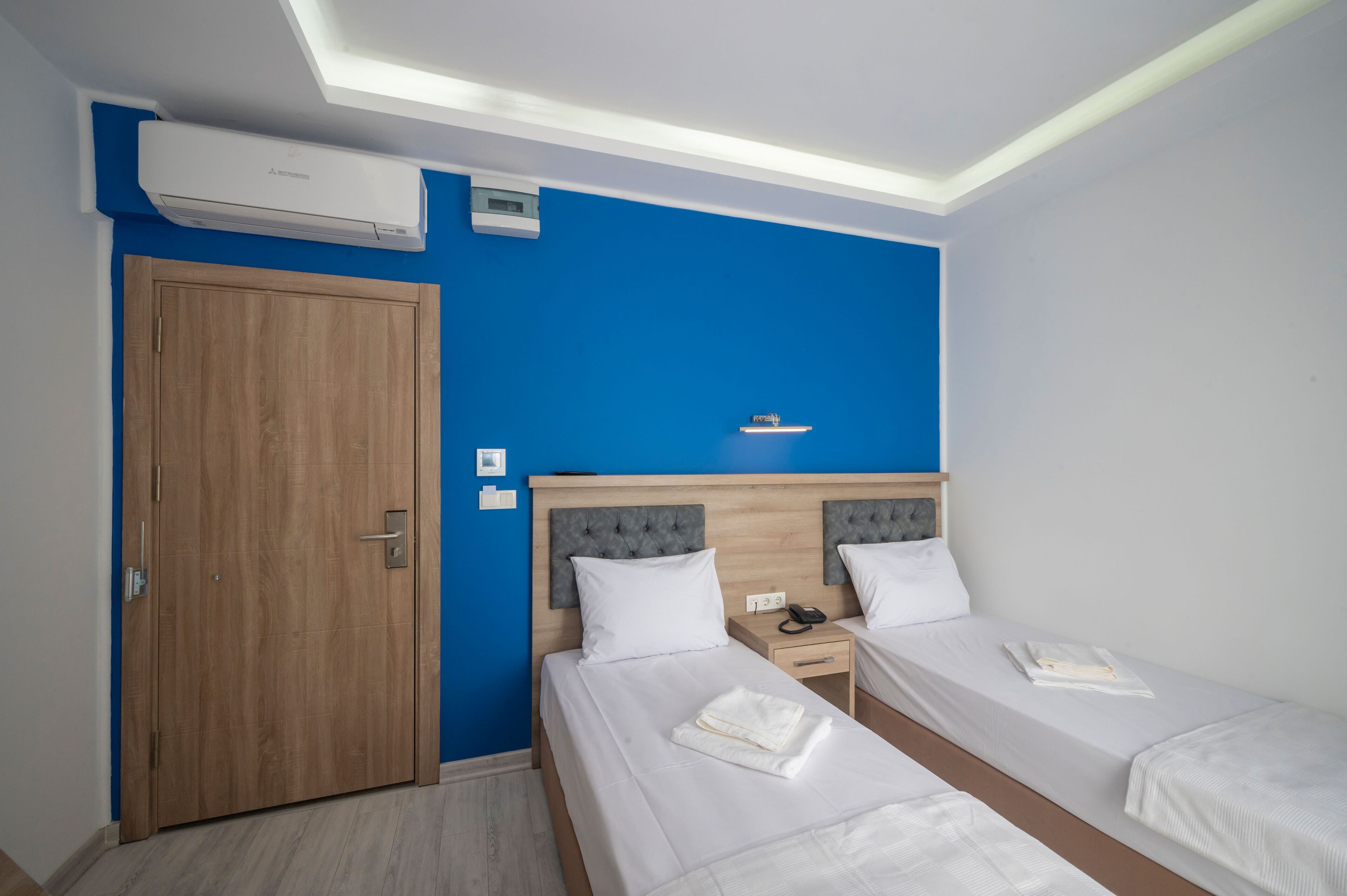 Habitación de hotel con dos camas, un armario de madera, una pared decorada en azul y un equipo de aire acondicionado.