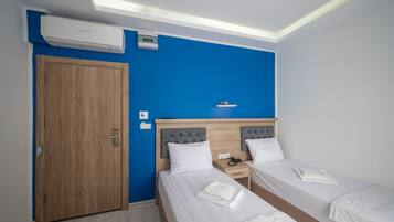 Habitación de hotel con dos camas, un armario de madera, una pared decorada en azul y un equipo de aire acondicionado.
