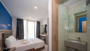 Una habitación de hotel con cama, mesita de noche y baño con lavabo y espejo.