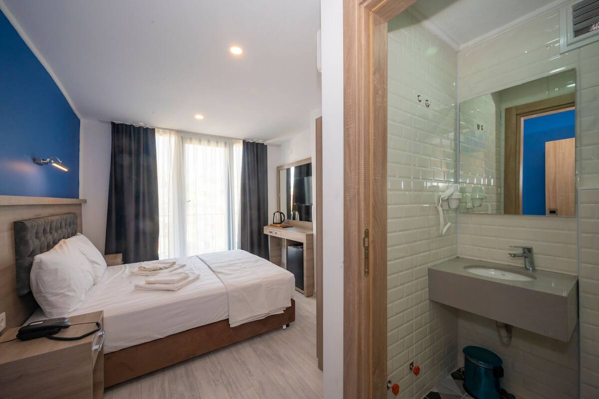 A hotel room with a bed, bedside table, and a bathroom with a sink and mirror.
