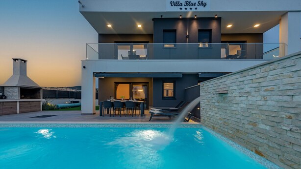 Una villa moderna con piscina, mobiliario exterior y chimenea.