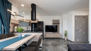Una sala de estar moderna con comedor, cocina y televisor montado en la pared.